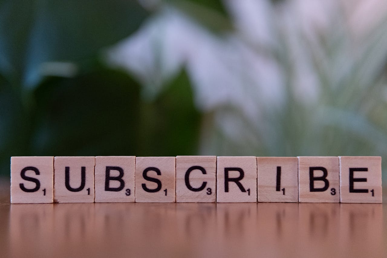 gallery-05 Close-up of the word SUBSCRIBE spelled with wooden letter tiles on a table.