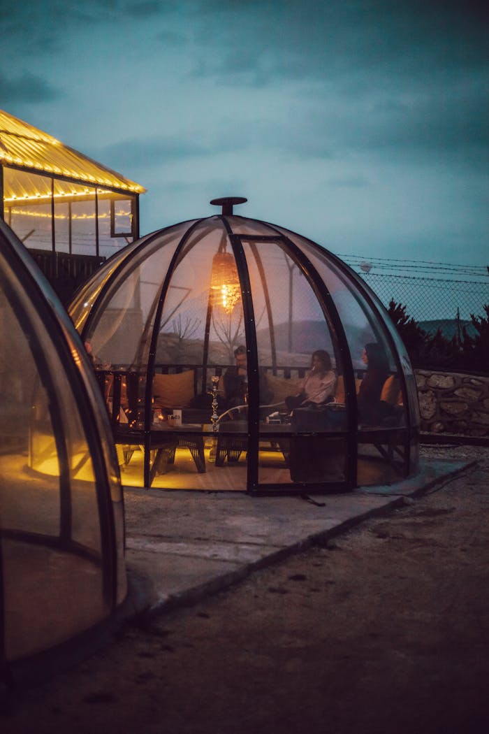 services-02 A person relaxes inside a warmly lit glass dome at night, showcasing modern architecture.