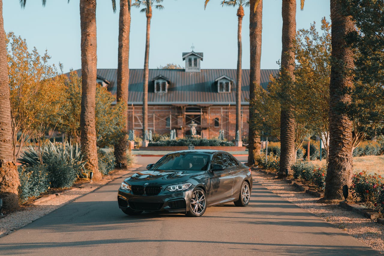 portfolio-01 A sleek BMW sports car parked along a picturesque tree-lined villa entrance, exuding luxury.